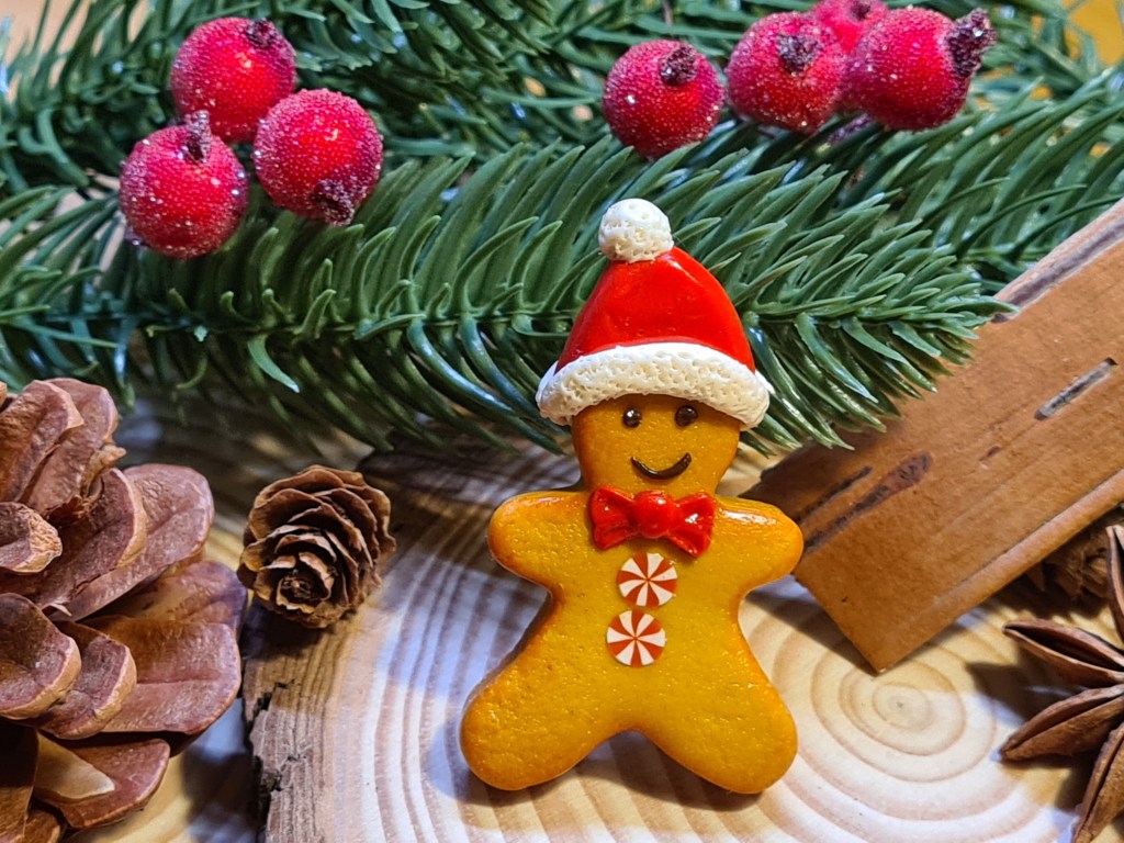 Broche petit bonhomme en pâte fimo. Le petit bonhomme porte un bonnet de père Noël rouge et blanc.
