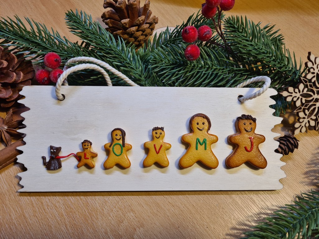 Plaque de porte en bois décorée d'une famille de petits biscuit composée de 5 personnages et d'un chien stylisé.